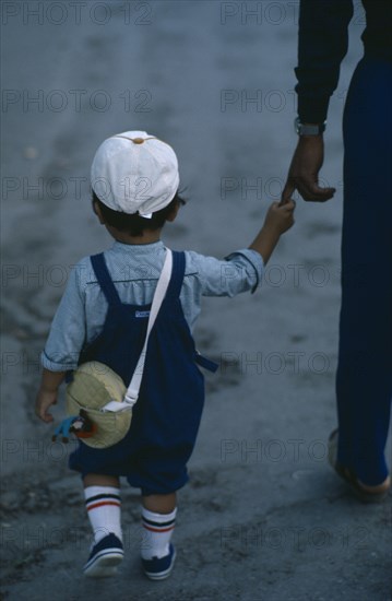 JAPAN, People, Children, "Young child seen from behind, wearing white cap and short trousers holding on to finger of adult, partly seen, at side."