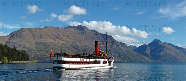 NEW ZEALAND, SOUTH ISLAND, OTAGO, "QUEENSTOWN, VINTAGE STEAMSHIP TSS EARNSALW LEAVING STEAMER WHARF AT QUEENSTOWN TAKING TOURISTS AND SAILING ON LAKE WAKATIPU WITH CECIL PEAK AND WALTER PEAK (FAR R) BEHIND."