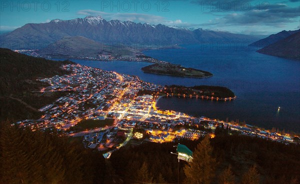 NEW ZEALAND, SOUTH ISLAND, OTAGO, "QUEENSTOWN, VIEW OF QUEENSTOWN AT DUSK WITH LAKE WAKATIPU AND REMARKABLES MOUNTAIN RANGE IN THE DISTANCE FROM THE SKYLINE RESTAURANT,CAFE AND GONDOLA COMPLEX ON BEN LOMOND ABOVE QUEENSTOWN."