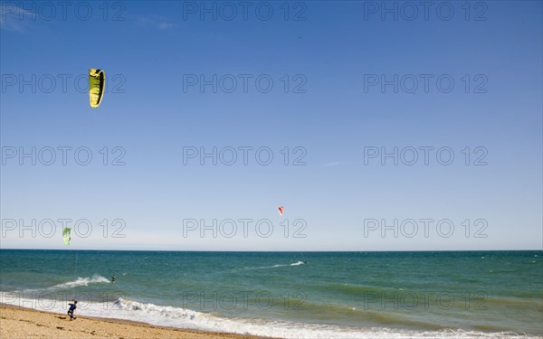 ENGLAND, West Sussex, Lancing, Kite Surfers on sea next to shingle beach in the summer with blue sky