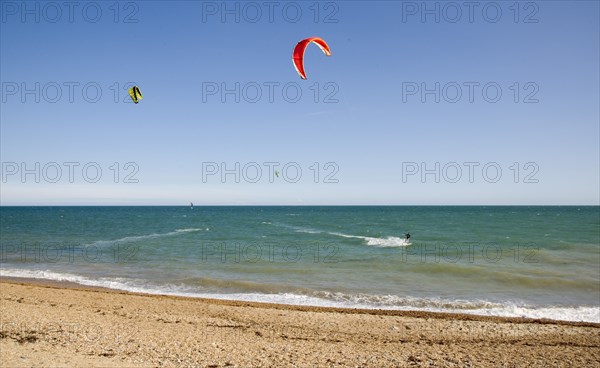 ENGLAND, West Sussex, Lancing, Kite Surfers on sea next to shingle beach in the summer with blue sky