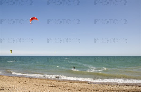 ENGLAND, West Sussex, Lancing, Kite Surfers on sea next to shingle beach in the summer with blue sky