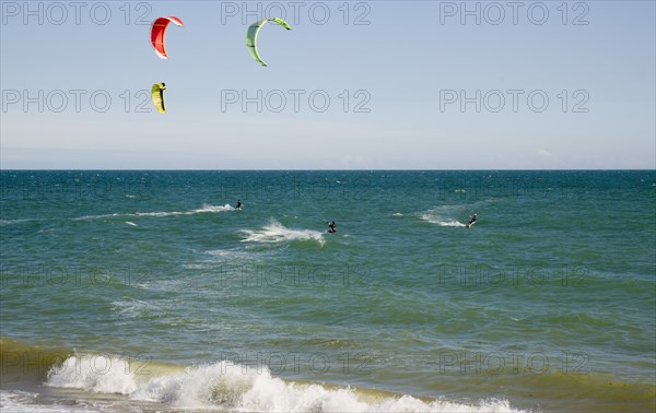 ENGLAND, West Sussex, Lancing, Kite Surfers on sea next to beach in the summer with blue sky