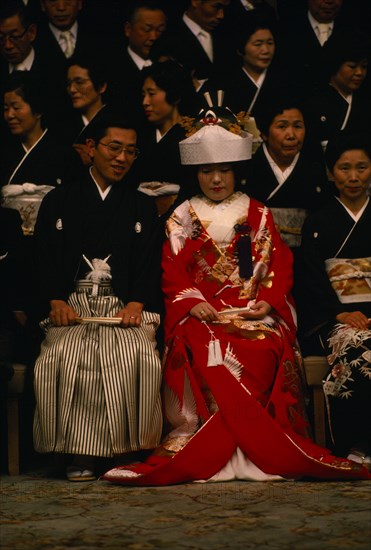 JAPAN, Honshu, Tokyo, Seated bride and groom and guests attending Shinto wedding ceremony wearing traditional dress before changing into western style clothes for later party.
