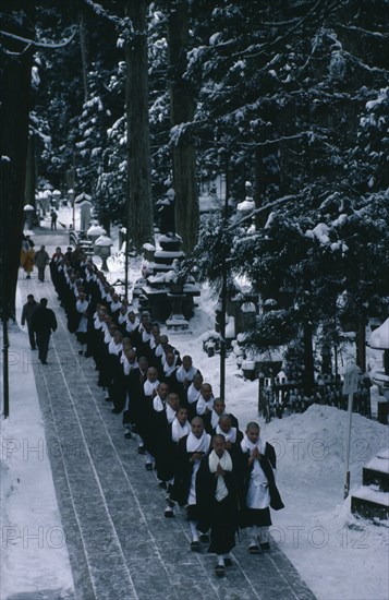 JAPAN, Honshu, Wakayama, Mount Koyosan.  Centre of the Shingon Buddhist sect established by the monk Kobo-daishi.  Novice monks dressed in black and white robes filing through forest of giant Cryptomeria trees in snow to make monthly obeisance at the mausoleum of Kobo-daishi.