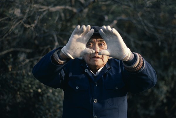 CHINA, Shanghai, "Man doing early morning T’ai Chi Chuan, the ancient Chinese discipline of physical training in a small riverside park.  Face partly framed by outstretched hands."