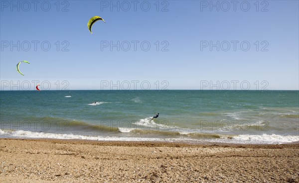 ENGLAND, West Sussex, Lancing, Kite Surfers on sea next to shingle beach in the summer with blue sky