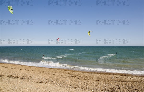 ENGLAND, West Sussex, Lancing, Kite Surfers on sea next to shingle beach in the summer with blue sky