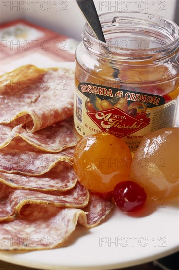 ITALY, Lombardy, Cremona, "Open jar of Mostarda di Cremona and salami.  Type of fruit preserve spiced with mustard essential oil, also known as mostarda di frutta."