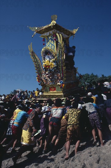 INDONESIA, Bali, Kuta, "Crowd carrying body of deceased to burning ground in highly decorated cremation tower where it will be transferred to a wooden bull which transports the soul to Paradise and everything will be burnt.  Bali’s religion is a blend of spirit worship, Buddhism and Hinduism."