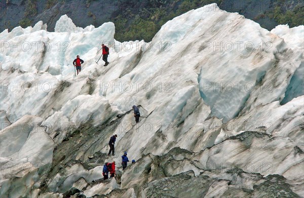 NEW ZEALAND, SOUTH ISLAND, WEST COAST, "MOUNT COOK NATIONAL PARK, A GROUP HIKES THE FRANZ JOSEF GLACIER. Julius von Haast, geologist and explorer, named Franz Josef Glacier in 1863, after the Emperor of the Austro-Hungarian Empire. Approximately 7000 years old, and a remnant of a much older and larger glacier which originally swept right to the sea, Franz Josef Glacier extends 12 kilometres from its three feeder glaciers in the high snow fields of the southern Alps."