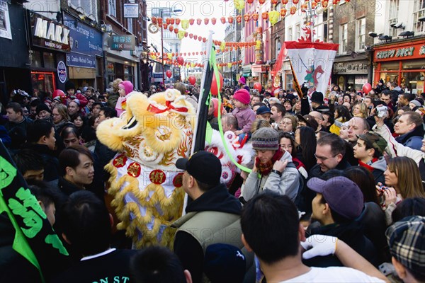 ENGLAND, London, Chinatown, Crowds passing under paper lanterns hung around one of the oriental ornamental gates or paifang in Gerrard Street following an embroidered banner during Chinese New Year celebrations in 2006 for the coming Year of The Dog