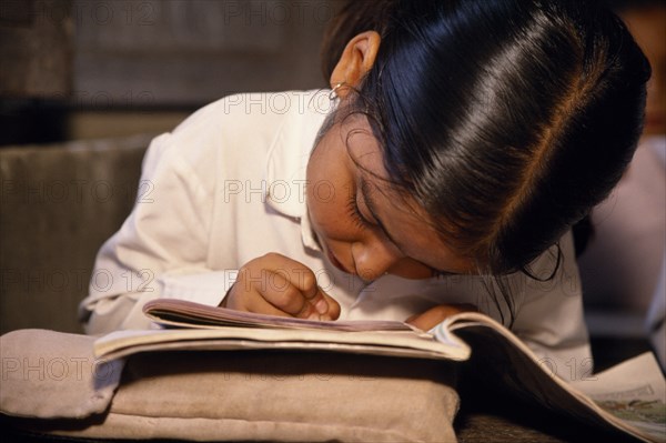 NEPAL, Dhulikhel, "Little girl, head bent forward in concentration over exercise books in primary school class."