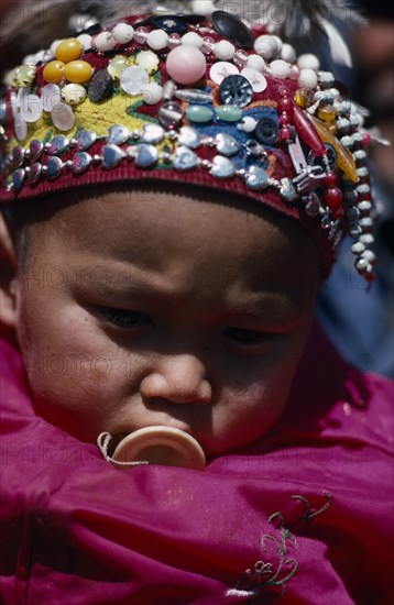 CHINA, Xinjiang Province, Altai Region, Portrait of Kazakh baby wearing hat covered with silver beads and coloured buttons.
