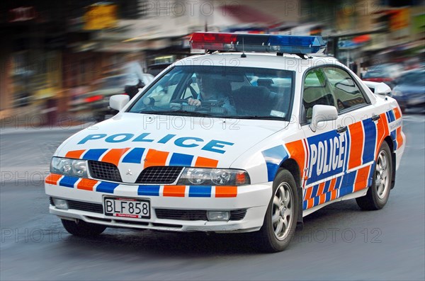 NEW ZEALAND, SOUTH ISLAND, OTAGO, "QUEENSTOWN, A NEW ZEALAND POLICE CAR AND OFFICER SPEEDS PAST ALONG SHOTOVER STREET, QUEENSTOWN."