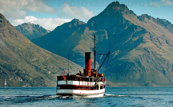NEW ZEALAND, SOUTH ISLAND, OTAGO, "QUEENSTOWN, VINTAGE STEAMSHIP TSS EARNSALW LEAVING STEAMER WHARF AT QUEENSTOWN TAKING TOURISTS AND SAILING ON LAKE WAKATIPU WITH WALTER PEAK BEHIND."