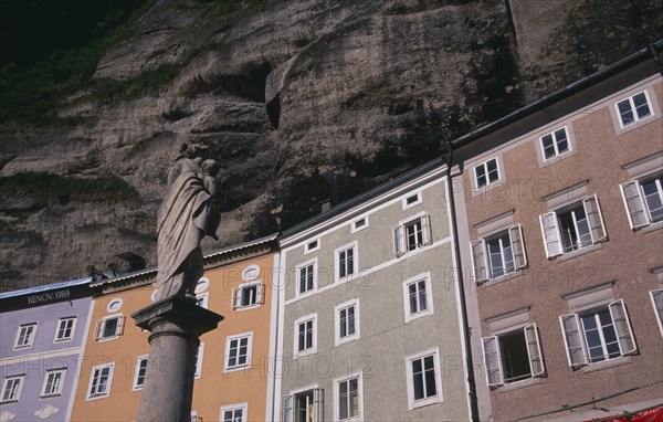 AUSTRIA, Salzburg, Pastel coloured houses on Gstatiengasse built into the Monchsberg beneath the fortress with statue on plinth in foreground.