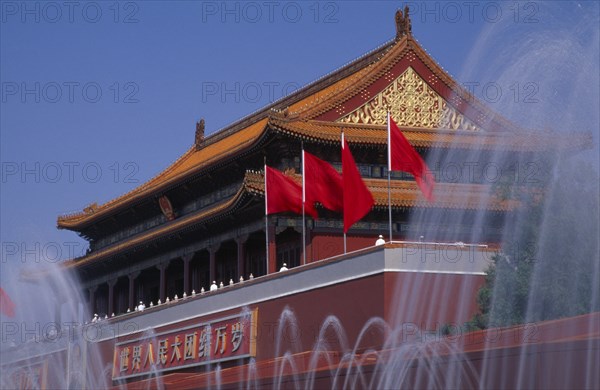 CHINA, Beijing, "Fountains and entrance gateway to the Forbidden City with red flags and red and gold decorated, tile pavilion-style rooftop .  "
