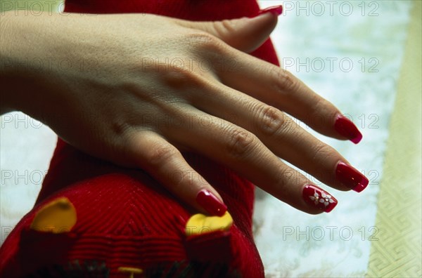 CHINA, Beijing, "Close cropped shot of manicured and painted nails with red nail polish, white flower detail and jewel type additions."