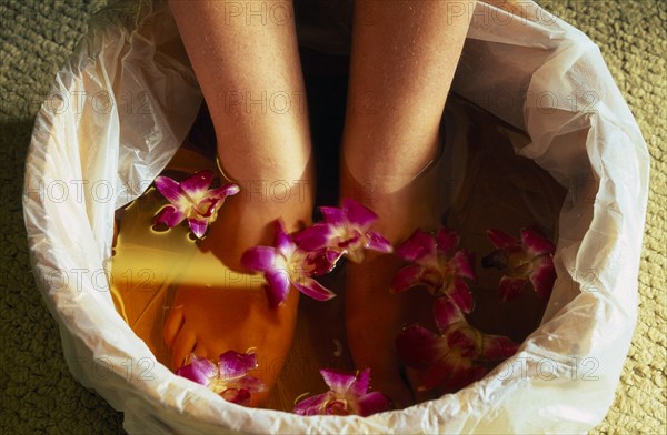 CHINA, Beijing, Bodhi Theraputic Retreat.  Close cropped shot of feet soaking in water scattered with orchid flowers.