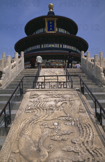 CHINA, Beijing, Tiantan Park.  Stone walkway and view up steps towards the Hall of Prayer for Good Harvests with visitors looking at tiered and decorated exterior.