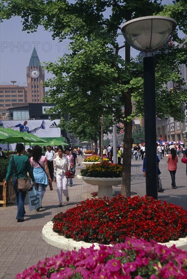 CHINA, Beijing, "Wangfujing street with crowds of shoppers lined with trees, street lamps and raised circular flower beds."