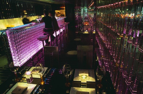 CHINA, Beijing, Tou Ming Si Kao ( TMSK ) bar interior with couple sitting at glass bar illuminated with coloured light.  Table laid with glasses and cutlery and lit by candles in foreground.