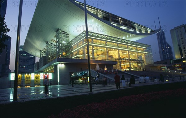 CHINA, Shanghai, "Opera House, Renmin Square.  Glass fronted exterior facade and upwardly curving roof illuminated at night with people standing or sitting in courtyard outside."