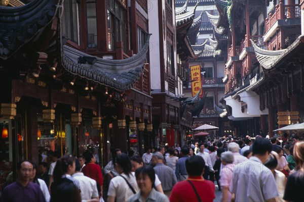 CHINA, Shanghai, "Yu Gardens, Old City.  Crowds of shoppers in narrow street lined with shop fronts with pagoda style rooftops."