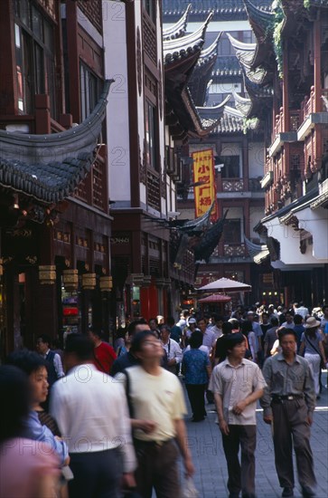 CHINA, Shanghai, "Yu Gardens, Old City. Crowds of shoppers on narrow street lined by buildings with pagoda style tiled rooftops."