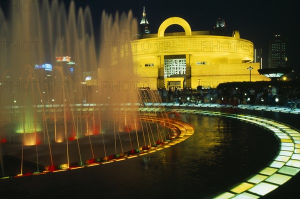 CHINA, Shanghai, "Shanghai Museum of Chinese Culture, Renmin Square.  Exterior and part view of circular fountain illuminated at night.  People standing or sitting around fountain."