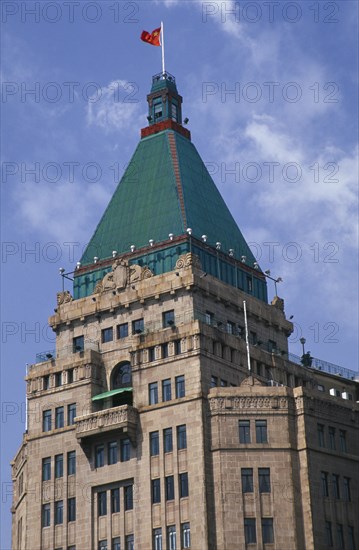 CHINA, Shanghai, The Peace Hotel on the Bund.  Detail of exterior tower with green rooftop and Chinese flag flying from the top.