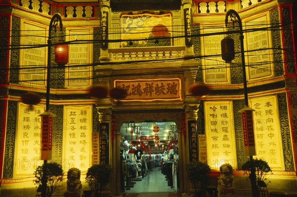 CHINA, Beijing, "Silk Emporium on Dazhalan Jie, exterior facade illuminated at night with open entrance and view inside over shop floor."