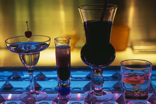 CHINA, Beijing, Tou Ming Si Kao (TMSK) bar.  Cocktails on glass bar illuminated blue and purple.