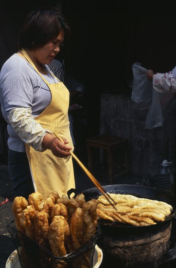 CHINA, Shanghai, "Woman using long pair of chopsticks to turn frying food in large, shallow dish in front of her."