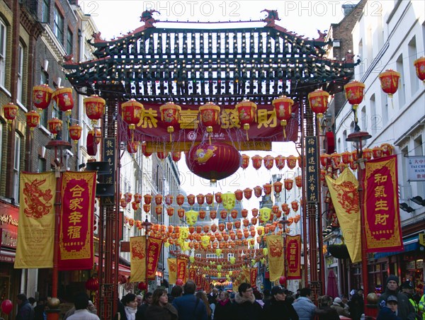 ENGLAND, London, Chinatown, Crowds passing under paper lanterns hung around one of the oriental ornamental gates or paifang in Gerrard Street during Chinese New Year celebrations in 2006 for the coming Year of The Dog