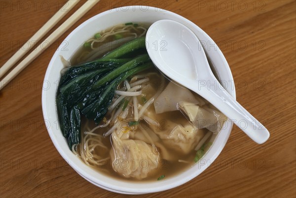 CHINA, Shanghai, Wonton soup.  Dumplings in a vegetable broth in bowl with spoon and chopsticks.