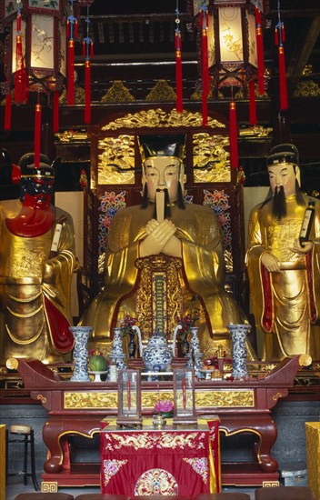 CHINA, Shanghai, "Yu Gardens, Temple of the City of God.  Three golden statues behind small altar with candles and incense and decorated lanterns hanging above. "