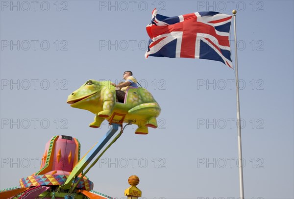 ENGLAND, West Sussex, Littlehampton, Families enjoying amusement ride at Harbour Park. British Union Jack flag Flying against a blue sky