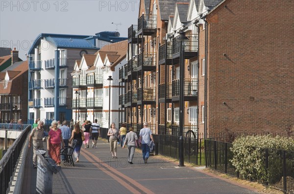 ENGLAND, West Sussex, Littlehampton, People walking along pathway next to the River Arun below harbour side housing developments