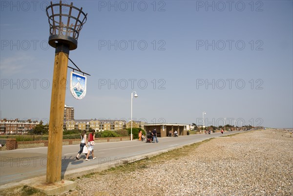 ENGLAND, West Sussex, Littlehampton, People walking along the promenade next to shingle beach with a torch beacon in the foreground