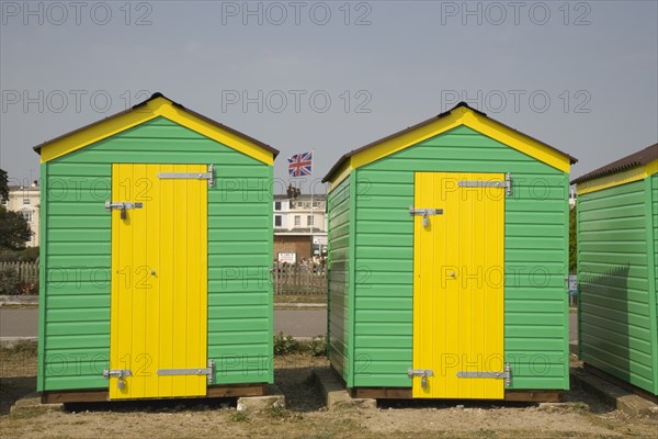 ENGLAND, West Sussex, Littlehampton, Green and yellow beach huts next to promenade with a Union Jack flag seen behind