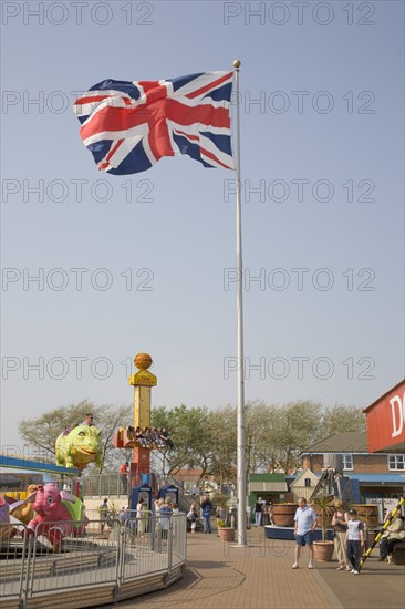 ENGLAND, West Sussex, Littlehampton, Harbour Park Amusements with families enjoying rides.  British Union Jack flag flying in the wind against a blue sky