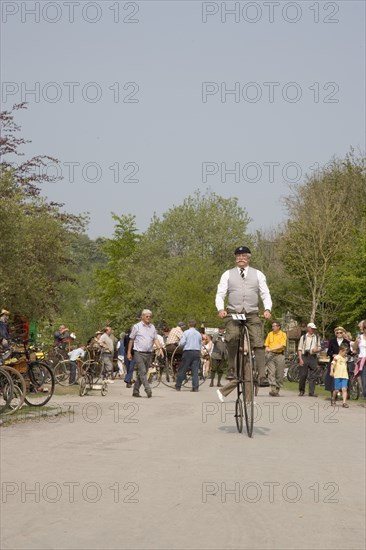 ENGLAND, West Sussex, Amberley, Amberley Working Museum. Veteran Cycle Day Grand Parade. Man wearing period custom riding a Penny Farthing bicycle with visitors watching.
