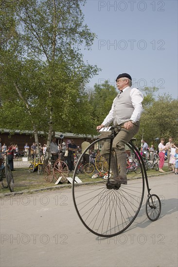 ENGLAND, West Sussex, Amberley, Amberley Working Museum. Veteran Cycle Day Grand Parade. Man wearing period custom riding a Penny Farthing bicycle with visitors watching.