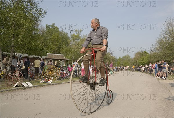 ENGLAND, West Sussex, Amberley, Amberley Working Museum. Veteran Cycle Day Grand Parade. Man wearing period custom riding a Penny Farthing bicycle with visitors watching.