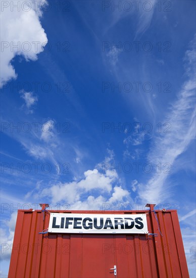 ENGLAND, West Sussex, Littlehampton, Red shipping container used as a lifeguards hut on the beach with expansive blue sky overhead