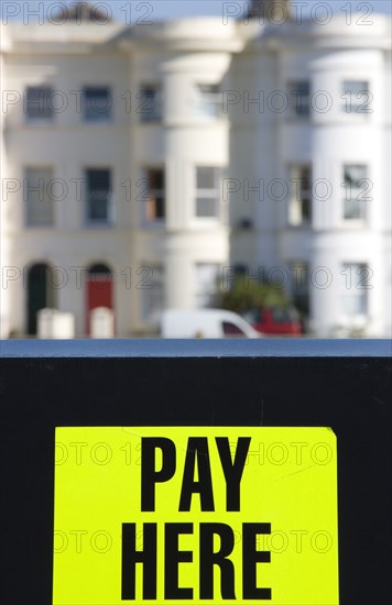 ENGLAND, West Sussex, Littlehampton, Yellow car park sign with black writing saying Pay Here with terraced seafront houses in the background