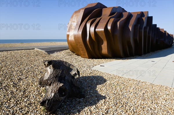 ENGLAND, West Sussex, Littlehampton, The rusted metal structure of the fish and seafood restaurant the East Beach Cafe designed by Thomas Heatherwick on the promenade with driftwood on the pebble beach in the foreground