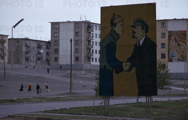MONGOLIA, Ulan Bator, Soviet billboard in central Ulan Bator  depicting Lenin shaking hands with Mongolia's first president Sukhebator in urban area with multi-storey apartment blocks behind and people crossing a central square . Ulaanbaatar East Asia Soviet Mongolia Asian Baator Male Men Guy Mongol Uls Ulaan